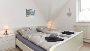 Une chambre avec un lit blanc, deux tables de chevet, une commode, une décoration en forme de cœur fixée au mur et une fenêtre.