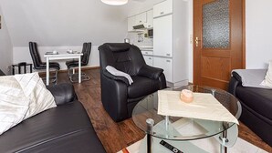 Un salon moderne avec une table basse en verre, un canapé en cuir, un fauteuil en cuir noir et un coin repas avec une table et des chaises blanches.