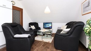 Une pièce moderne avec deux fauteuils de massage noirs, une petite table avec un ordinateur portable, un mur blanc et un luminaire suspendu.