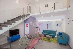 A modern living room with a staircase, a flat-screen TV, and a blue sofa. - Dandelion boutique hostel (Zadar)