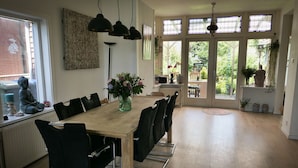 Un coin repas avec une table en bois, des chaises noires et des luminaires suspendus. Une fenêtre offre une vue sur la verdure à l’extérieur.