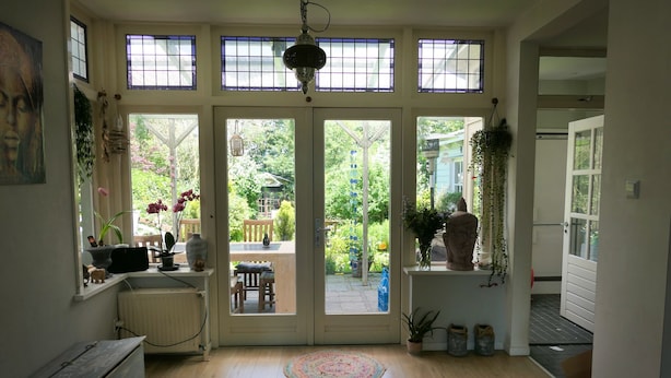 Une pièce avec un plancher en bois, un bureau avec un ordinateur, une chaise, une fenêtre donnant sur un jardin et un luminaire suspendu.