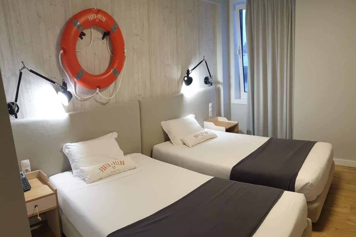 Une chambre d’hôtel avec deux lits, une table de chevet avec un téléphone, un gilet de sauvetage accroché au mur et une fenêtre avec des rideaux.
