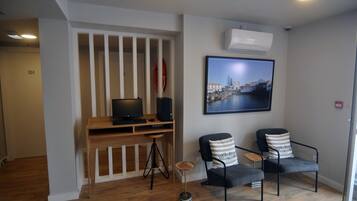 A room with a wooden desk, two chairs, a framed cityscape picture, and an air conditioning unit.