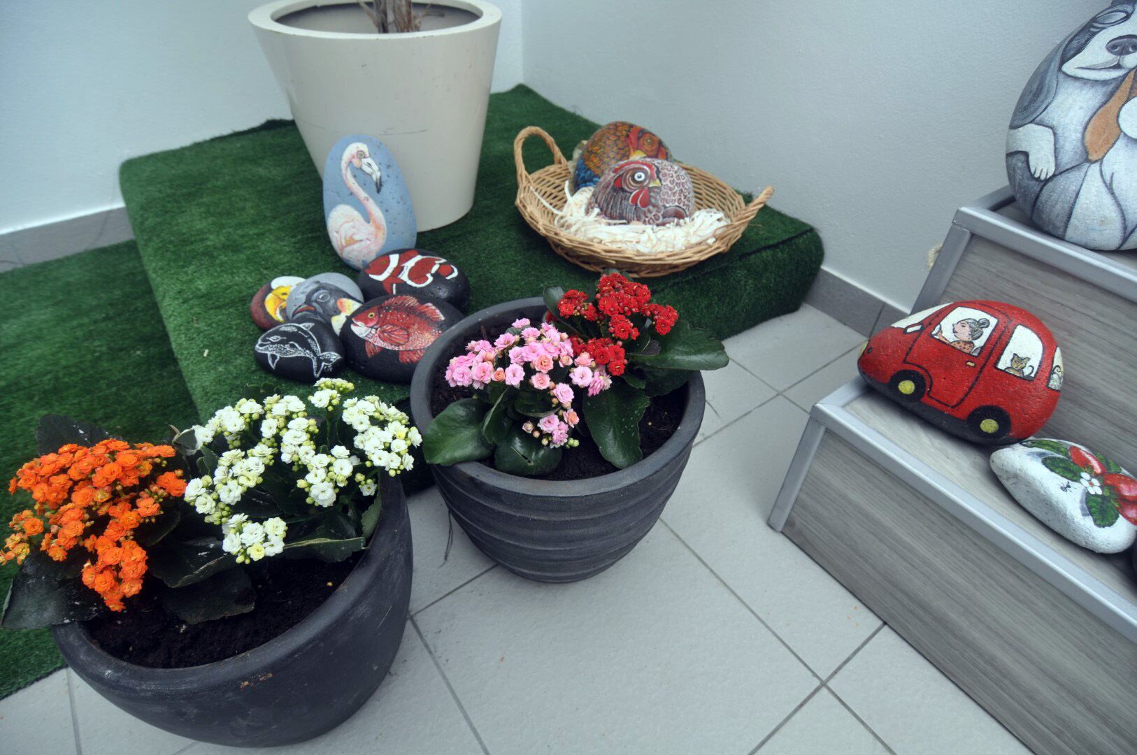 Plantas en macetas con flores, un flamenco pintado, una cesta con huevos y un coche pintado.