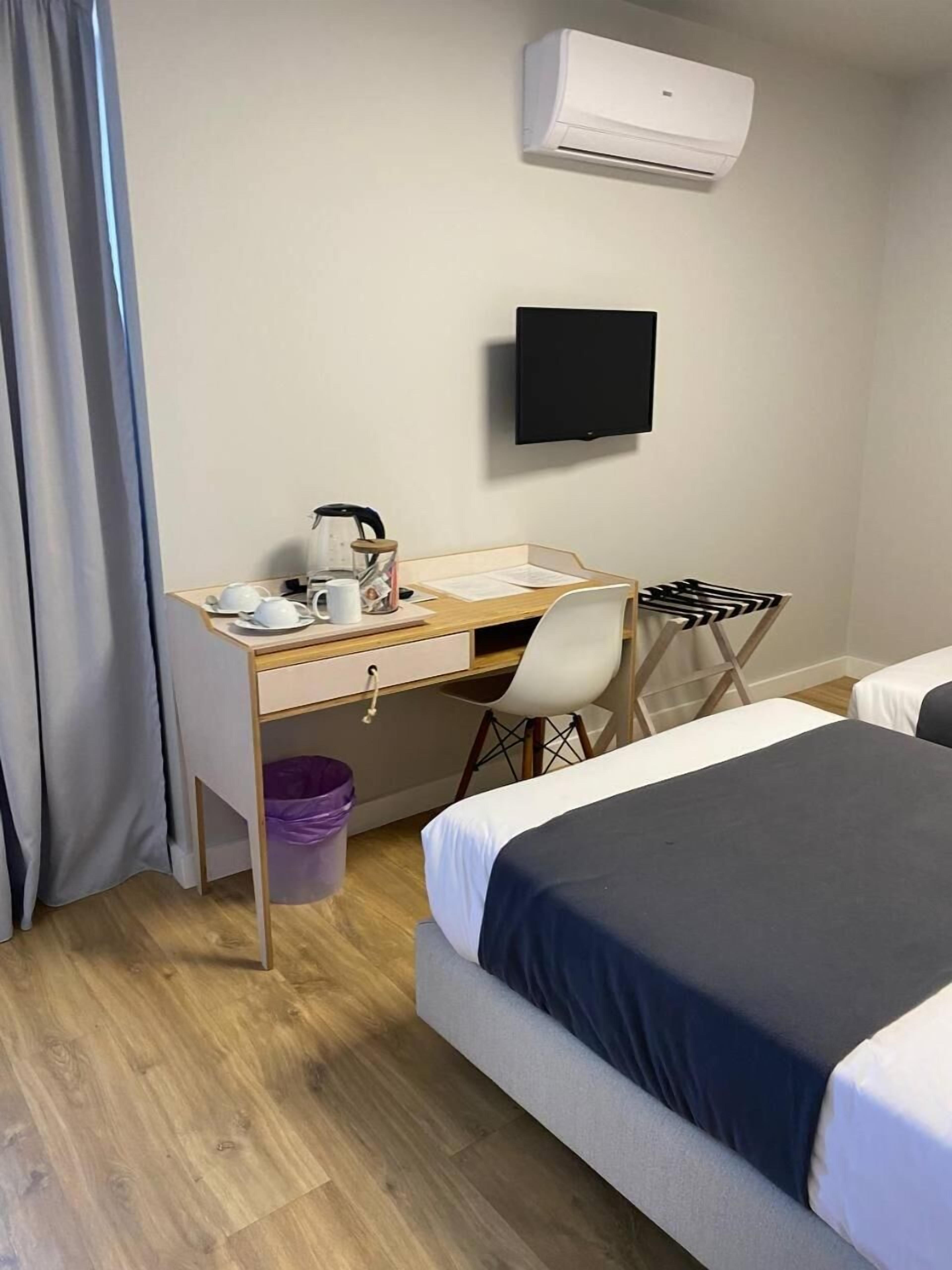 A hotel room with a bed, a desk with a chair, a television, and an air conditioning unit.