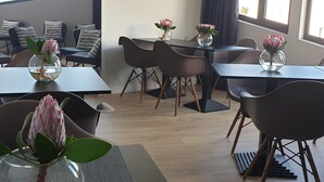 Een moderne hotelkamer met een zithoek, met een tafel met stoelen, een vaas met bloemen en een uitzicht op het landschap door grote ramen.