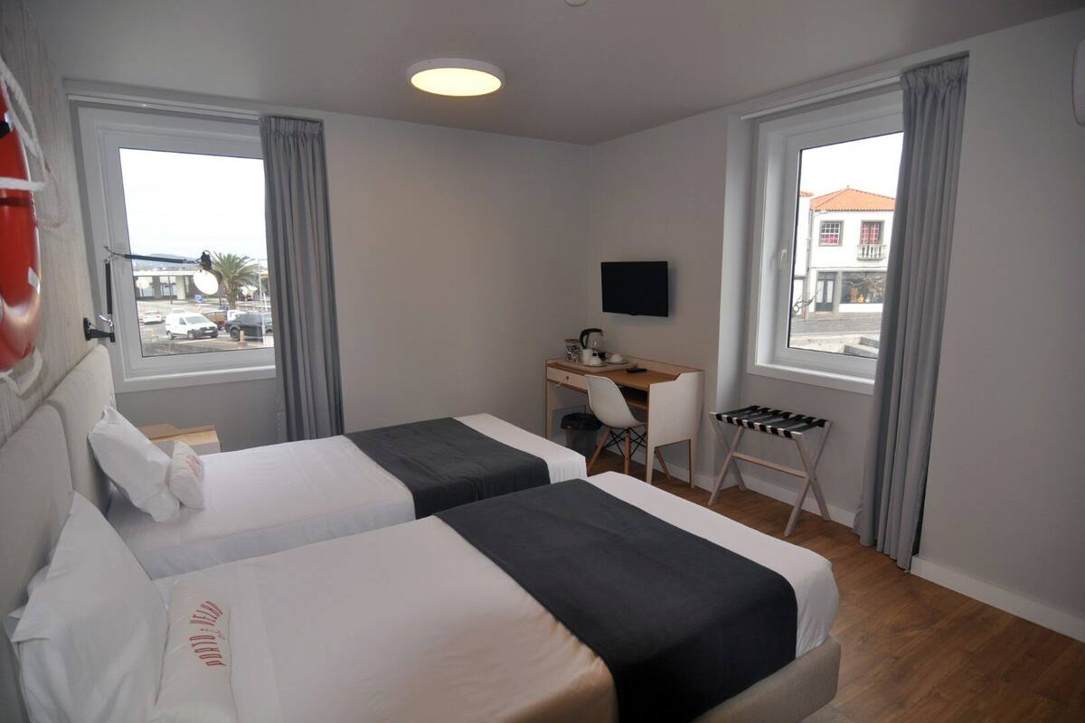 Une chambre d’hôtel avec deux lits, un bureau, une chaise, une télévision et de grandes fenêtres avec des rideaux.