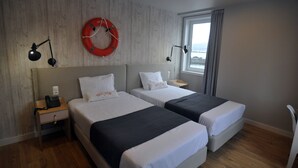 Een hotelkamer met twee bedden, een houten wand, een raam met uitzicht en een reddingsboei aan de muur.