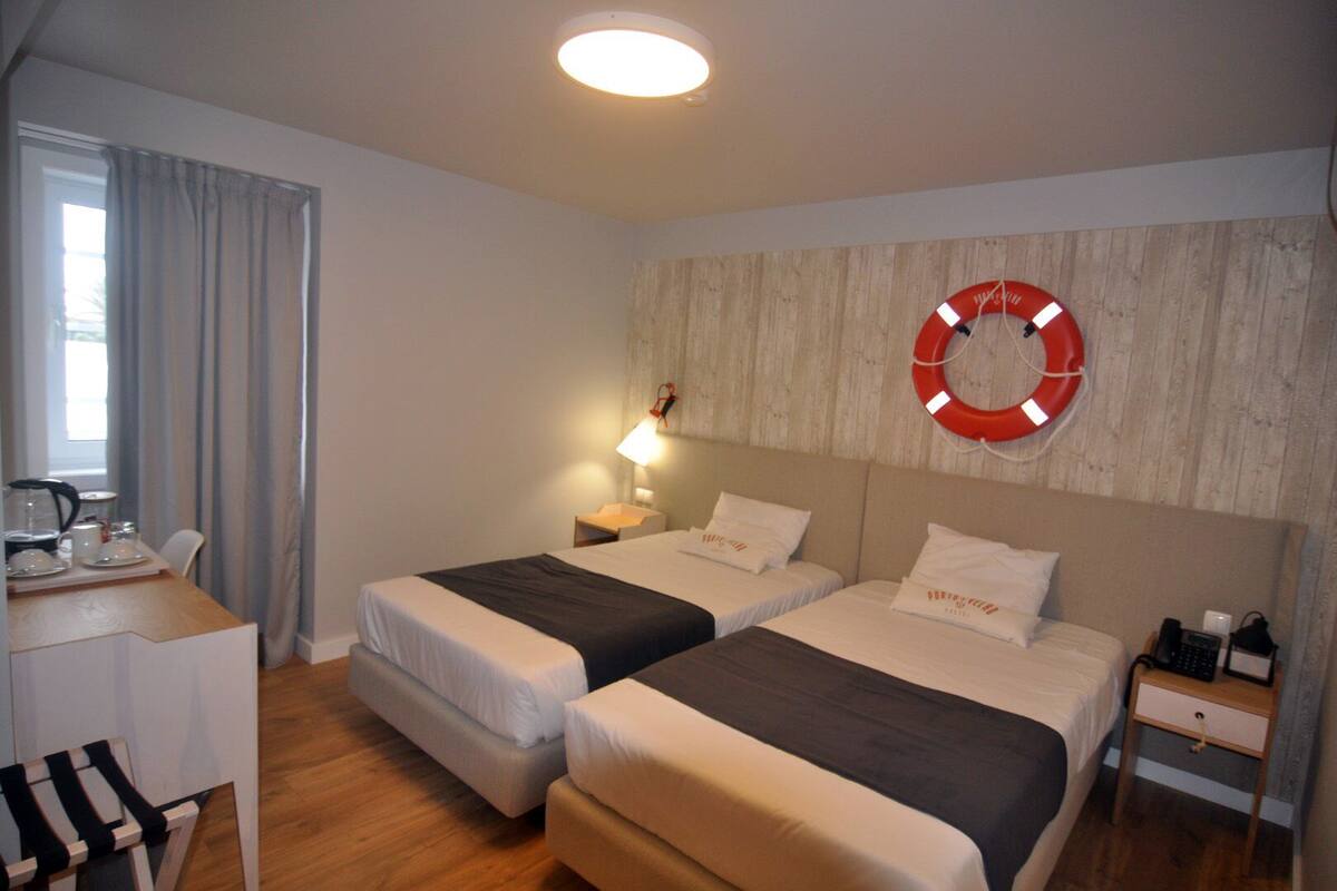 Une chambre d’hôtel avec deux lits, un bureau doté d’une machine à café, une lampe et un anneau de sauvetage accroché au mur.