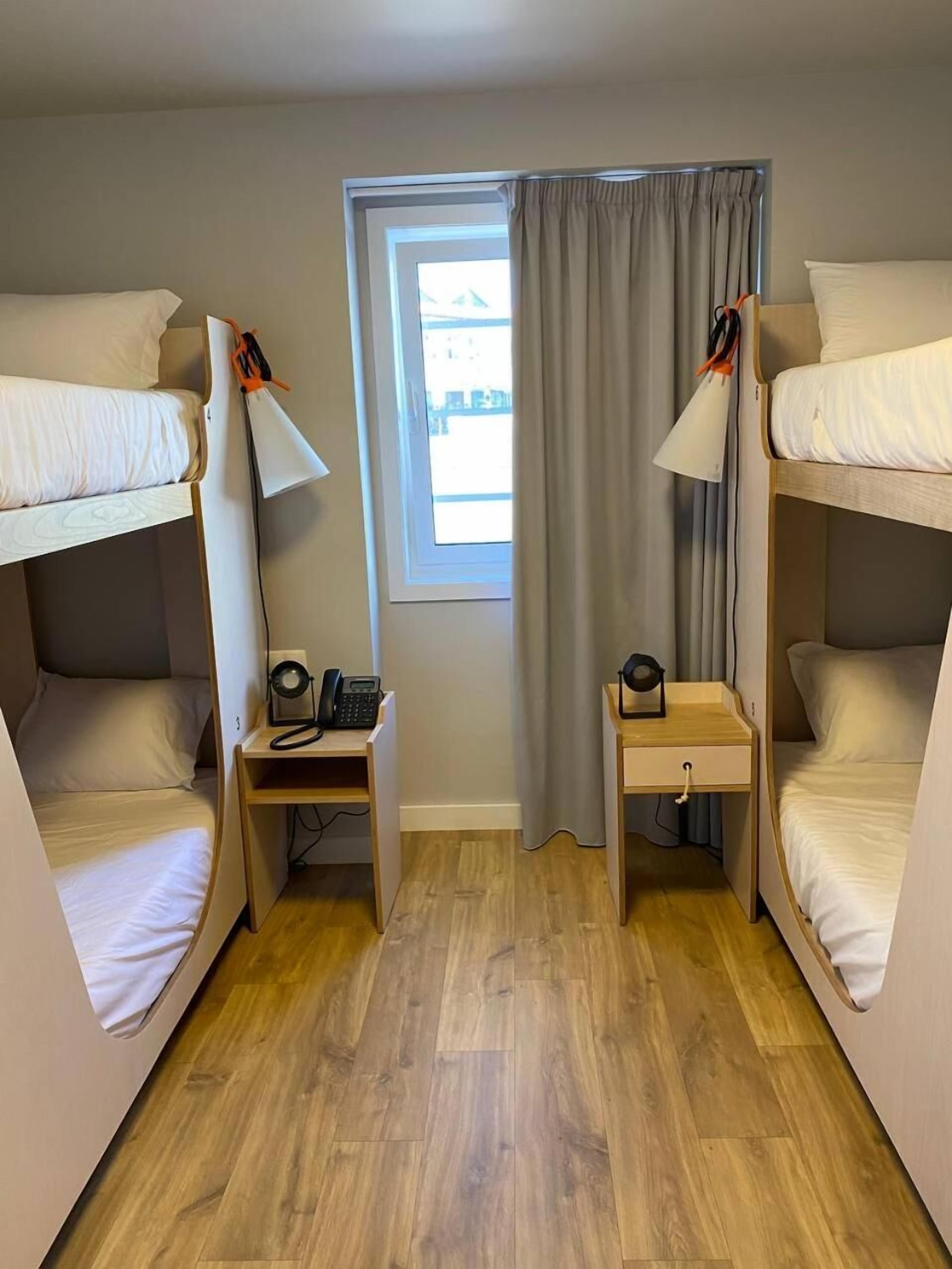 Une petite chambre comprenant deux lits superposés, un petit bureau avec une lampe et une fenêtre avec des rideaux.