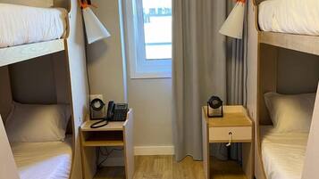 Una habitación compacta con dos literas, un escritorio pequeño con lámpara y una ventana con cortinas.