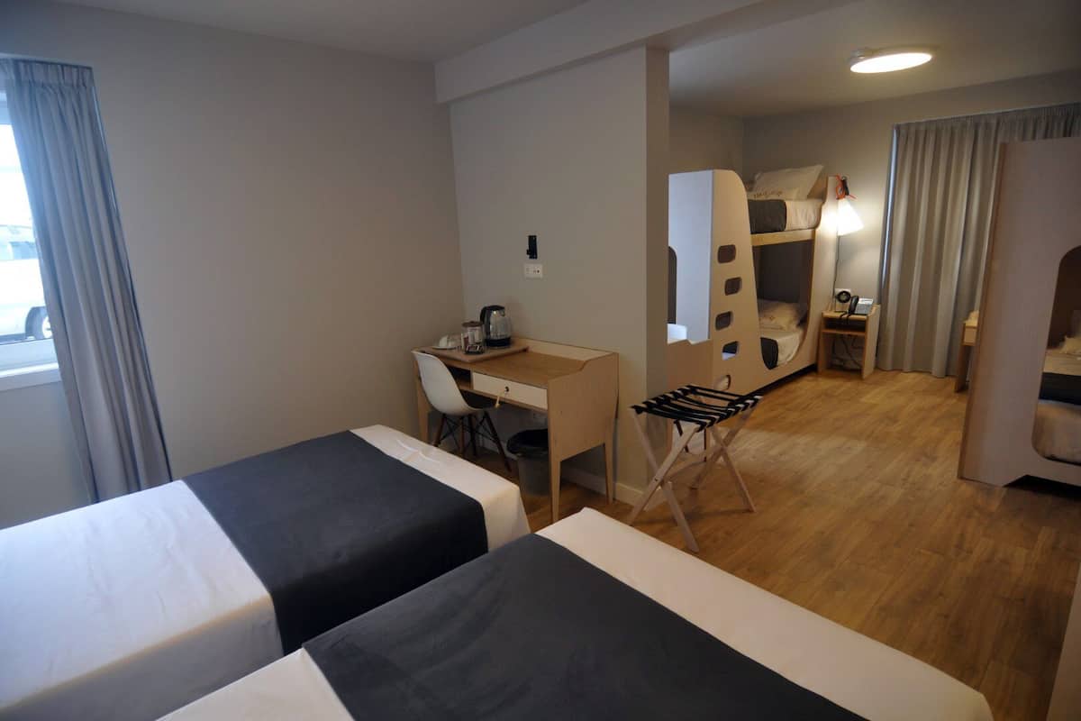 Une chambre d’hôtel avec deux lits, un bureau, une chaise, une petite table et, au fond, un lit superposé.