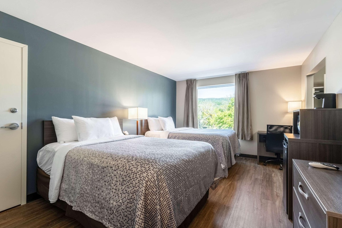 A hotel room with two beds, a desk, a chair, and a window with curtains.