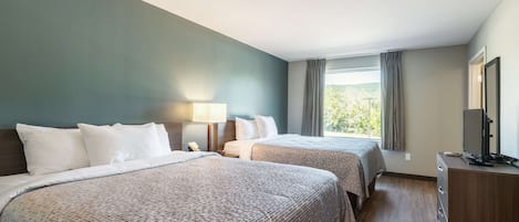 A hotel room with two beds, a desk, a TV, and a window with curtains.