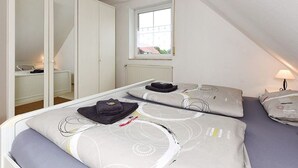 Une chambre avec deux lits, une armoire, une fenêtre et un radiateur.