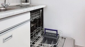 Une cuisine avec un plan de travail blanc, une machine à café, un lave-vaisselle et un égouttoir à vaisselle.