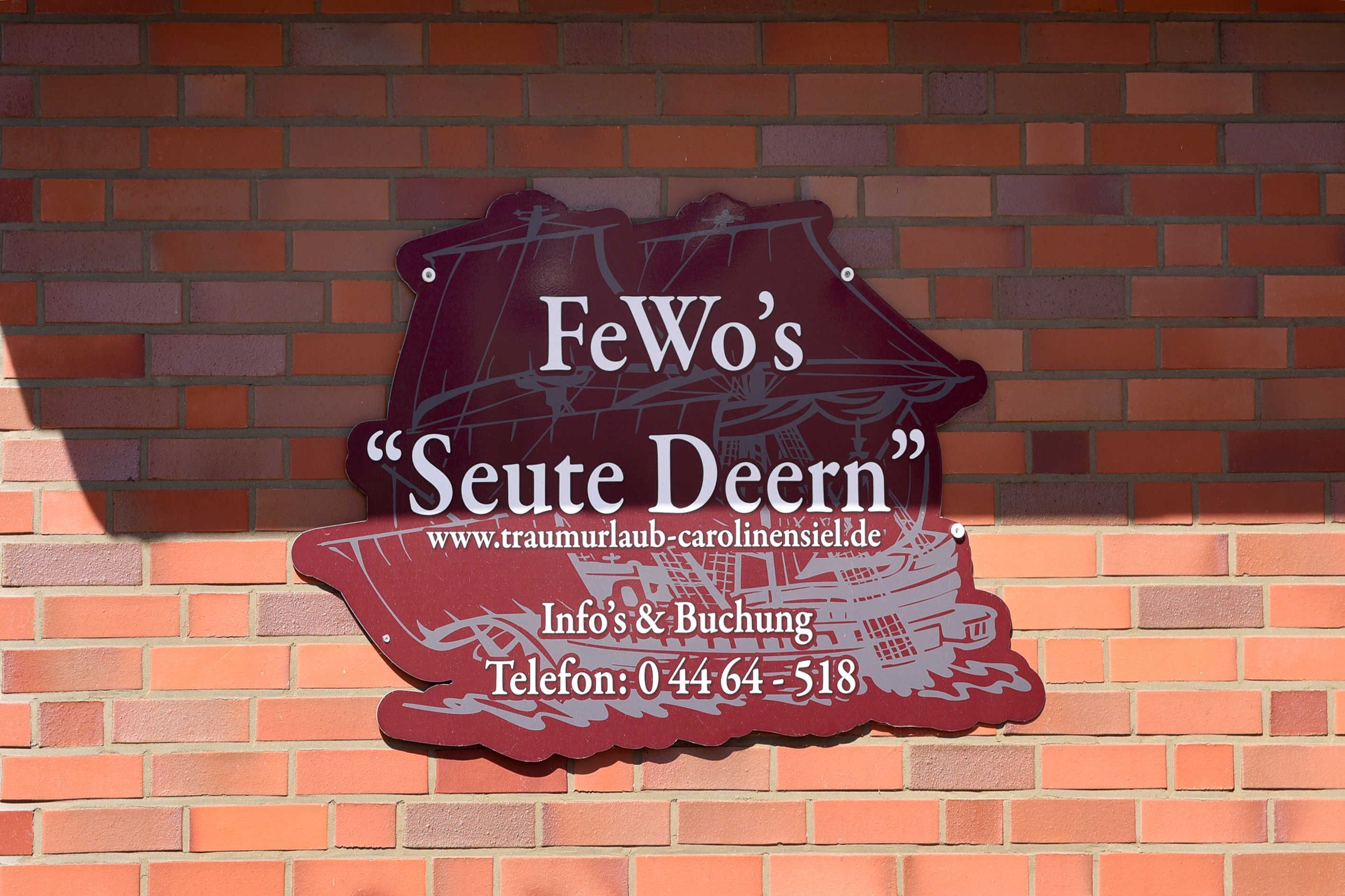 A sign with the text "FeWo's 'Seite Deern' www.traumurlauf-carolinensiel.de Info's & Buchung Telefon: 04464-518".