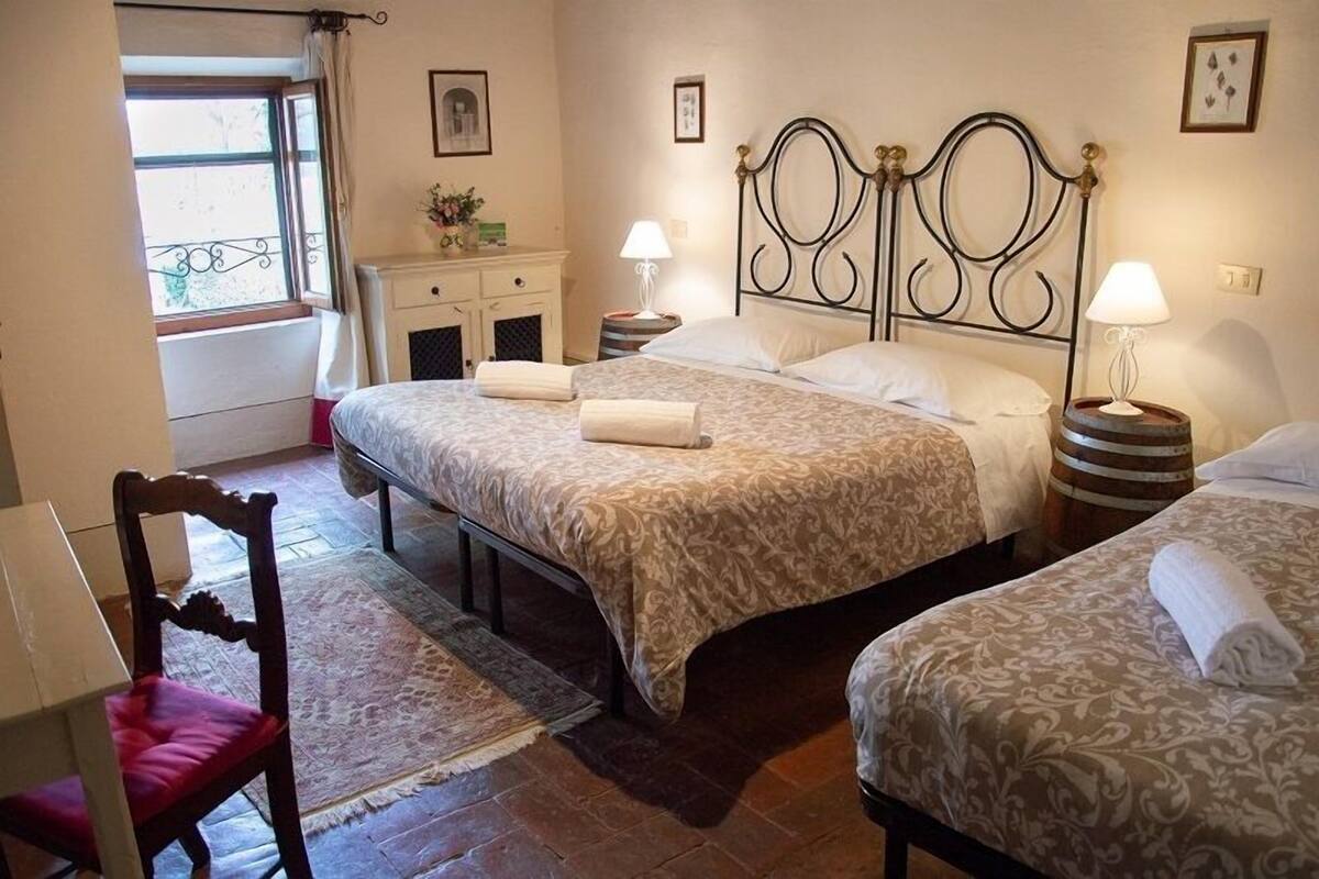Une chambre avec deux lits, une chaise en bois, une table de chevet, une lampe et une fenêtre donnant sur un beau paysage.