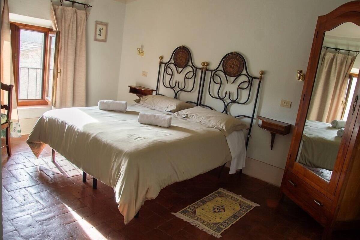 Une chambre à coucher avec un grand lit, une commode en bois, un miroir et une fenêtre avec des rideaux.