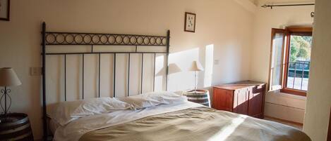 Un dormitorio con una cama, una mesita de noche de madera, una lámpara, una ventana y un estante en la pared.