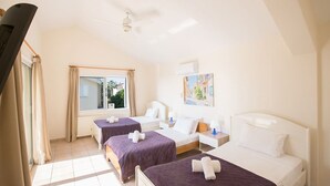 Habitación de hotel con dos camas, ventilador de techo, ventana con cortinas y aire acondicionado instalado en la pared.