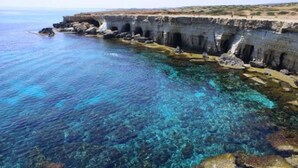 Una zona costera con aguas azul turquesa, formaciones rocosas y un muro de piedra con arcos.