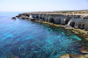 Una zona costera con aguas azul turquesa, formaciones rocosas y un muro de piedra con arcos.