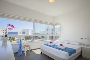 Quarto de hotel moderno com uma janela grande, cama com toalhas, uma cadeira e uma escrivaninha.