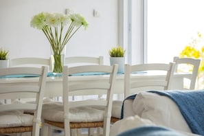 Uma área de refeições com cadeiras brancas, uma mesa com um vaso de flores e uma janela com luz natural.