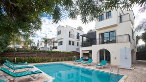 A swimming pool with lounge chairs, a covered patio, and a building with balconies. - Cyprus Villa Near the Beach, Protaras Villa 1244 (Paralimni)