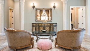 A grand foyer with two ornate armchairs, a central console table, and a large mirror above.