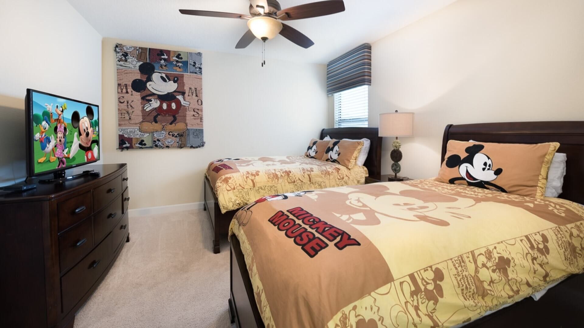 A bedroom with two beds, a ceiling fan, a television, and Mickey Mouse-themed decor.