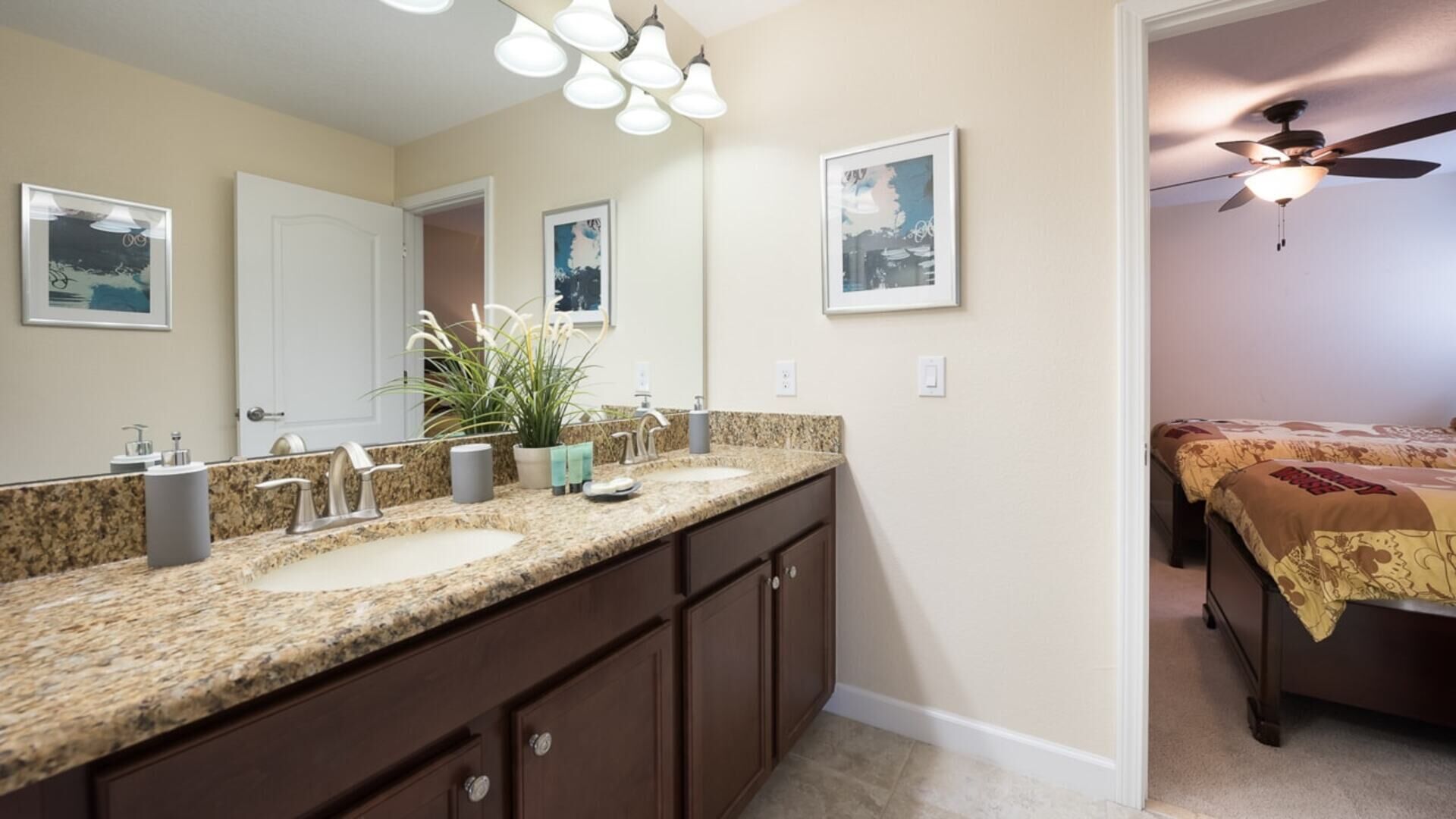 Une salle de bain avec un meuble-lavabo à deux vasques, un ventilateur de plafond et des tableaux encadrés accrochés aux murs.