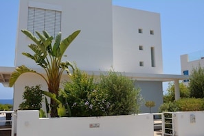 Um edifício moderno branco com varanda, cercado por vegetação exuberante e céu claro.