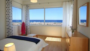 A bedroom with a large window, a bed, a bedside table, and a dresser. - Villa for Rent in Protaras 1029 (Paralimni)