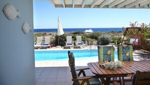 A poolside area with a view of the sea, lounge chairs, and a table with cups and saucers. - Villa for Rent in Protaras 1029 (Paralimni)