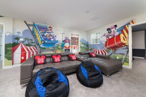 A room with a grey sectional sofa, bean bags, and a wall mural featuring cartoon characters. - Luxury 8 Bedroom Villa on Champions Gate Resort, Orlando Villa 3584 (Davenport)