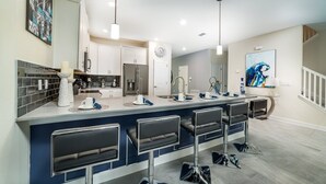 Una cocina moderna con una isla central, taburetes de bar y un comedor con un amplio ventanal.
