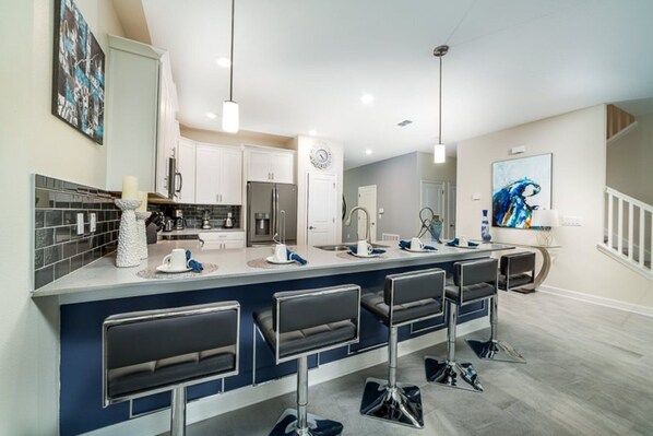 A modern kitchen with a central island, bar stools, and a dining area with a large window.