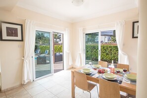 A dining area with a table set for four, a sliding glass door leading to a patio, and a framed picture on the wall. - Cyprus Villa Near the Beach, Protaras Villa 1245 (Paralimni)