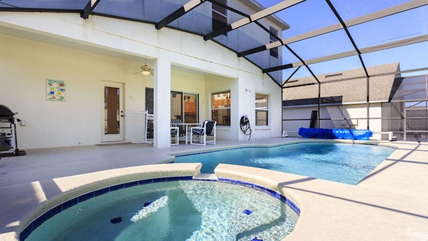 Una piscina interior con techo de cristal, un jacuzzi y una zona de patio con sillas y una parrilla.
