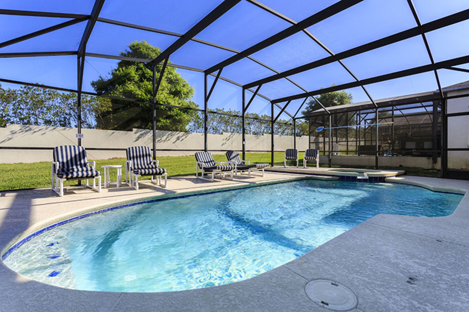 Une piscine dotée d’une enceinte en verre, entourée de chaises longues et d  ’une pelouse.