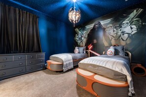 A bedroom with two beds, Star Wars-themed decor, a dresser, and a ceiling light.