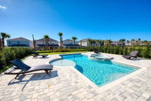 A swimming pool with lounge chairs, a hot tub, and a clear blue sky.
