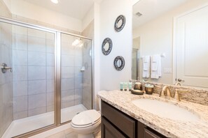 A bathroom with a glass shower enclosure, a white toilet, a vanity with a marble countertop, and three wall-mounted mirrors.