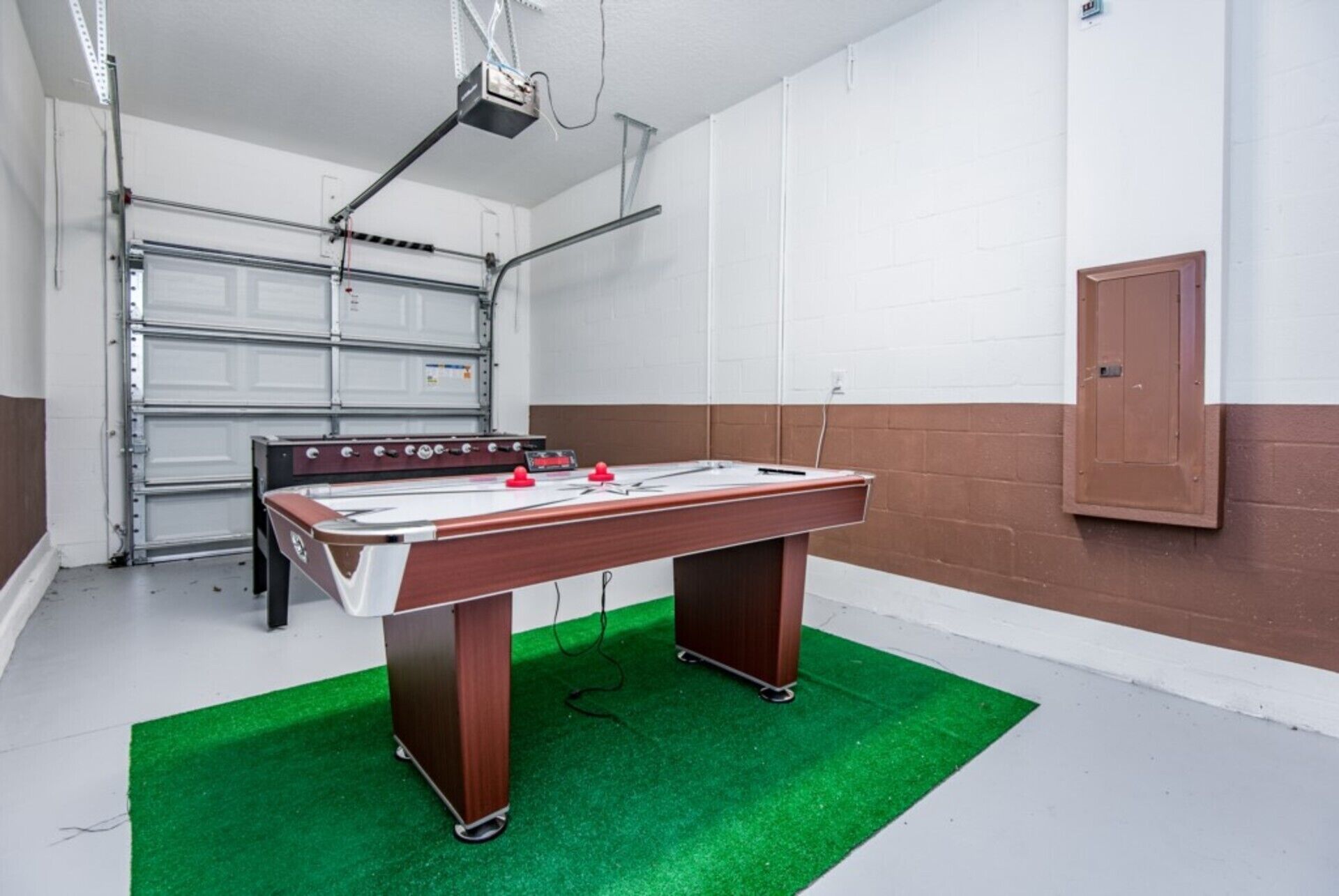 A foosball table in a room with a white and brown wall, a garage door, and a projector mounted on the ceiling.