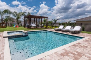 A rectangular swimming pool with a hot tub, surrounded by a brick deck. There are lounge chairs and a gazebo in the background.