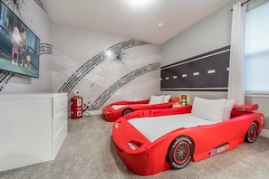 Une chambre avec un lit en forme de voiture de sport rouge, une grande télévision et une fresque murale.