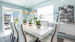 A modern dining area with a white table, white chairs, and three potted orchids. - Beautiful Villa With Private Pool, Close to Disney, Orlando Villa 2942 (Kissimmee)